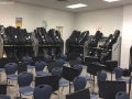 a classroom full of blue chairs and sheet music stands in the foreground, with shelves of guitars in the background