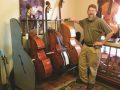 a bearded man standing next to a rack holding 3 double basses, placed on a carpet